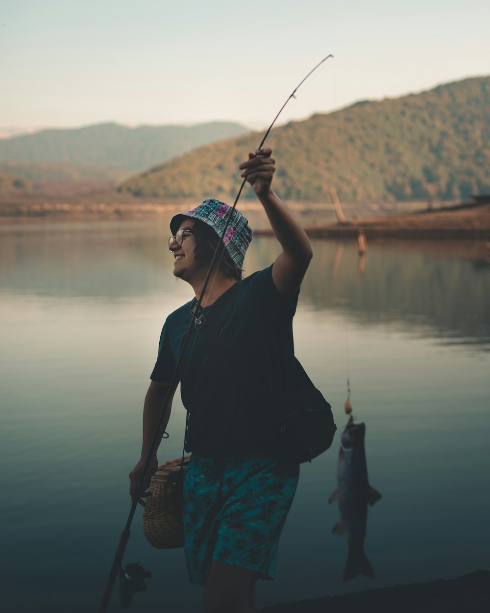 黒いシャツを着た男が湖のそばに立って釣り竿を持っている