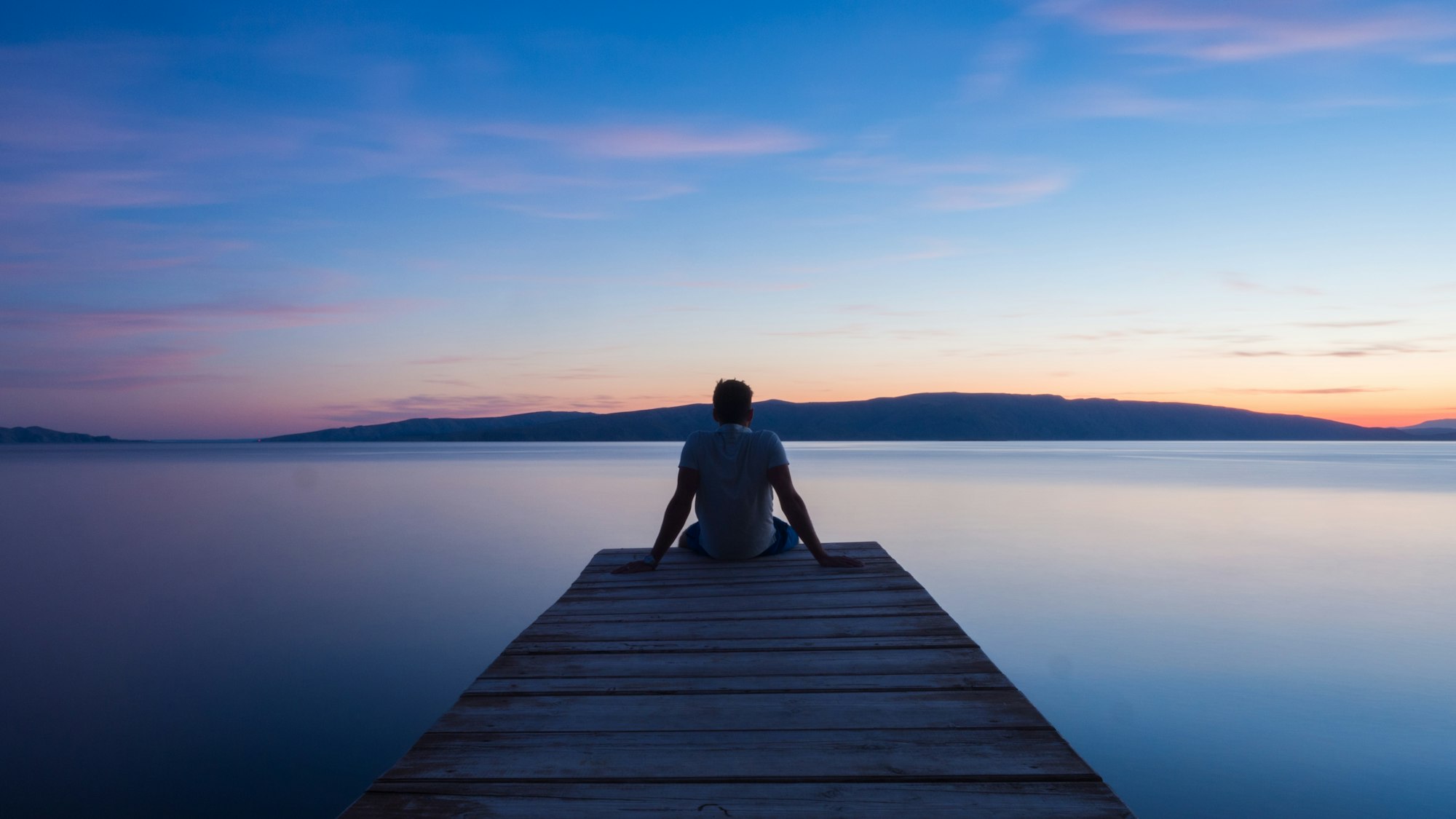 Man sitting on a wooden bridge overlooking a river.