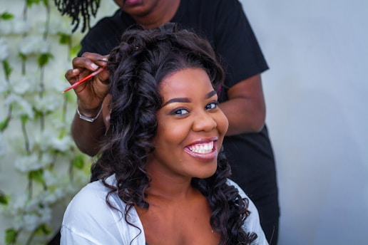 Close-up of a woman smiling with long, flowing natural hair extensions in a cozy salon setting.