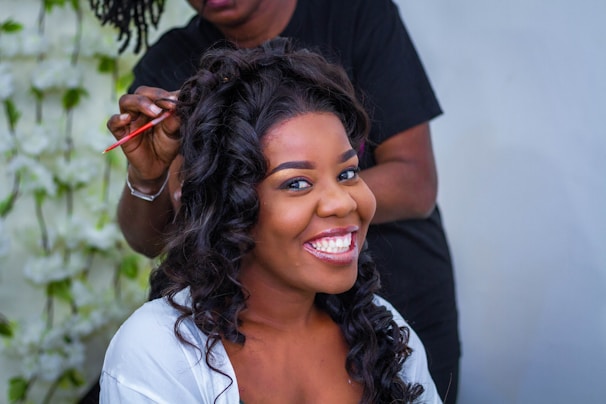 Smiling hair therapist applying a natural hair treatment on a client's curly hair in cozy salon setting