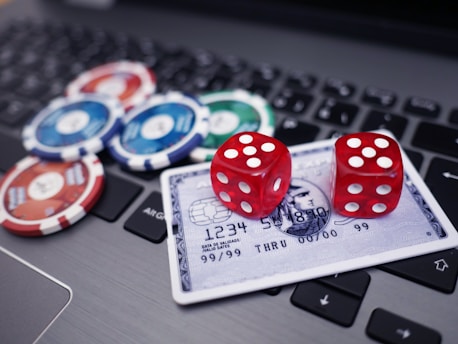 A set of red dice and poker chips are placed on top of a credit card, which is situated on a laptop keyboard. The poker chips are in various colors, including blue, green, red, and white.