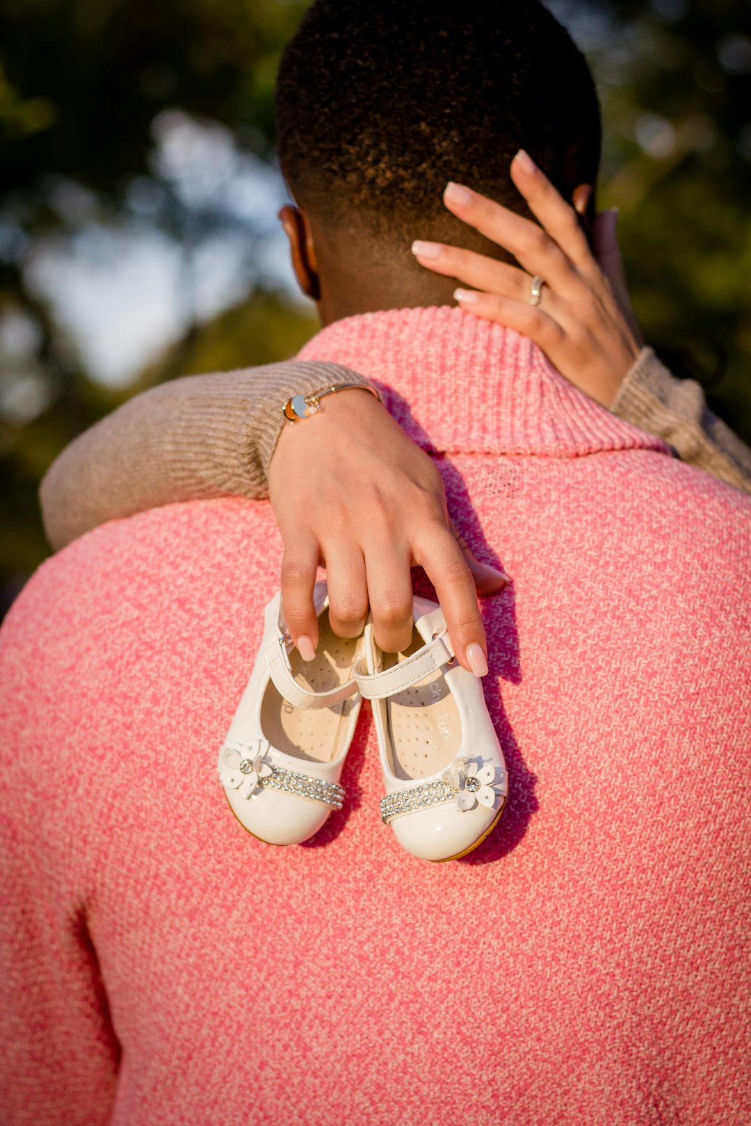 person holding baby's shoes in front of man wearing pink cardigan