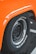 Close-up of a black tire with white lettering on the sidewall, set against an orange fender of a vehicle, with a parking lot surface visible beneath.