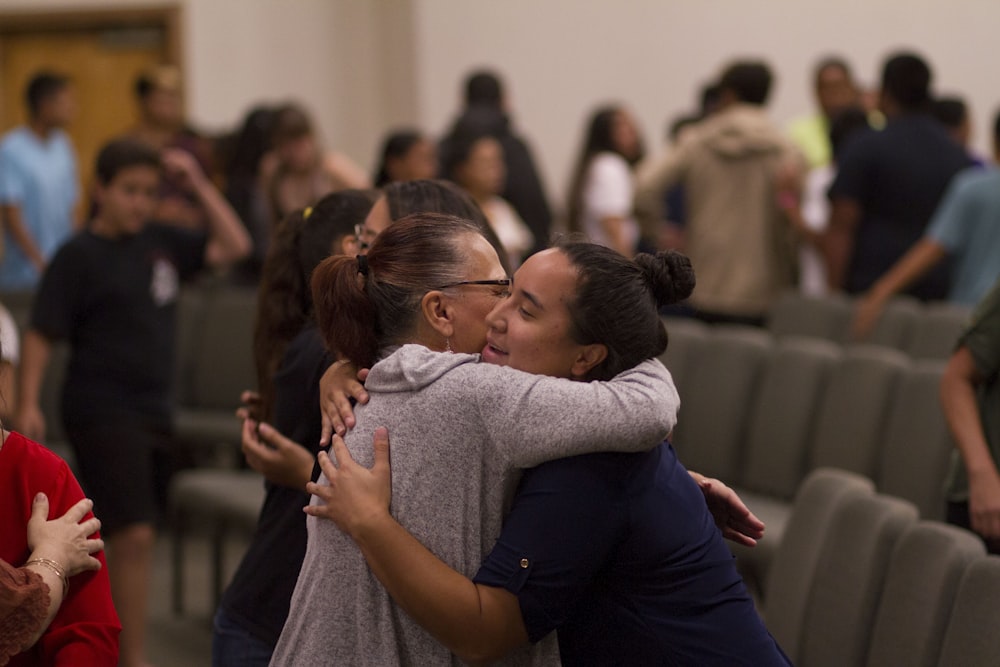 two women hugging each other in a room full of people