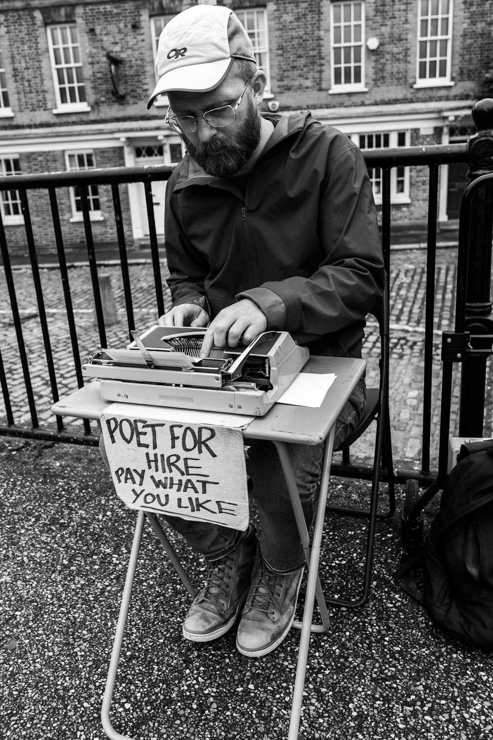 fotografia em tons de cinza do homem sentado e usando máquina de escrever
