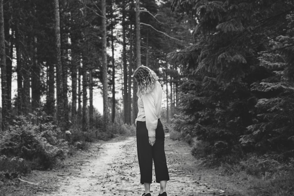 foto in scala di grigi di donna in piedi vicino a boschi e cespugli