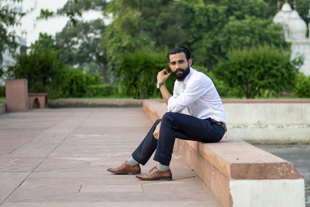 man in white dress shirt and blue jeans sitting on benc