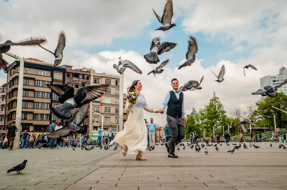 couple running surrounded by doves during daytime