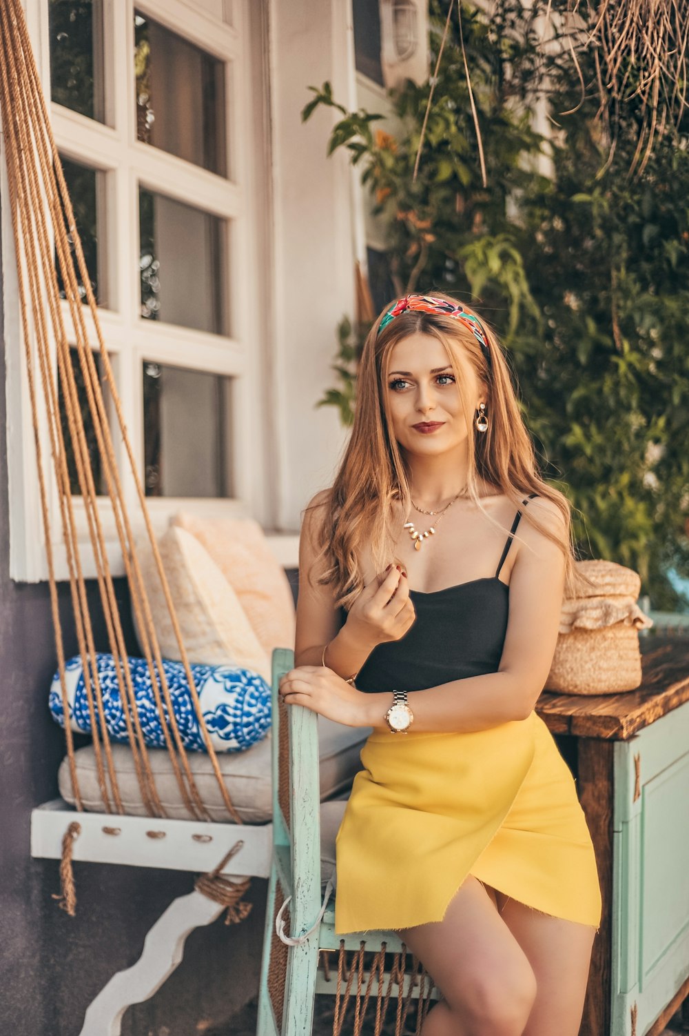 woman wearing black spaghetti strap top and yellow mini skirt standing near cabinet smiling