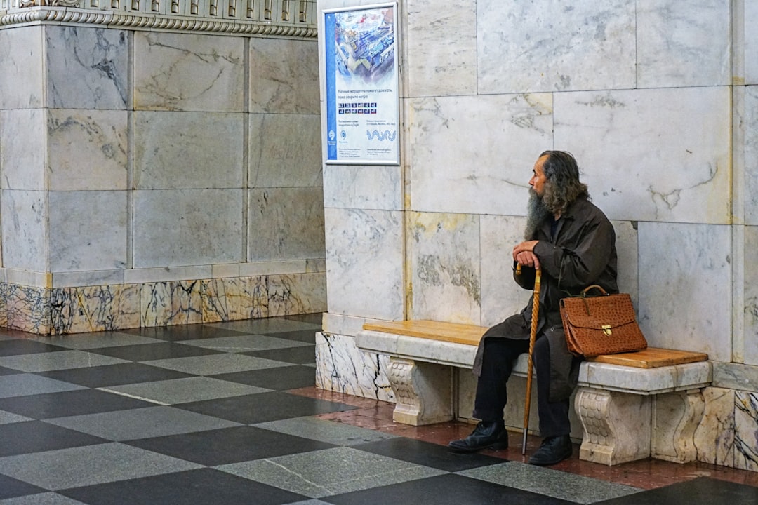 man wearing black trench coat and black pants sitting on bench