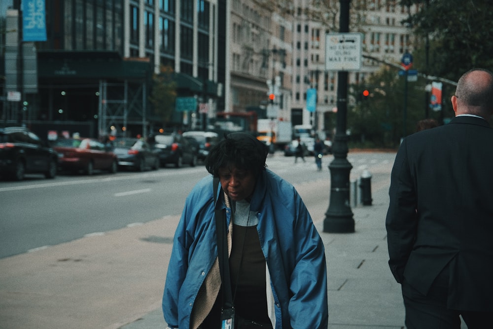 woman wearing blue jacket walking on pathway near another man viewing different vehicles on road during daytime