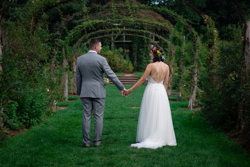 man and woman holding hands under arch near trees