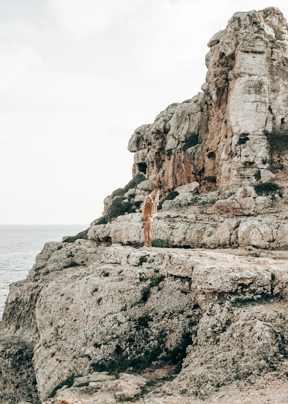 woman standing on rock formation facing on seashore during daytime