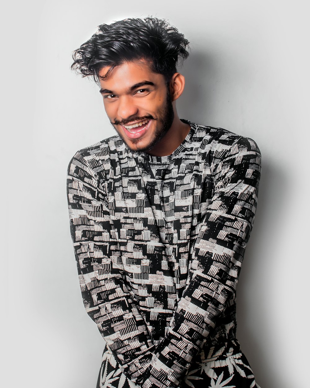 smiling man wearing grey long-sleeved shirt leaning on white wall