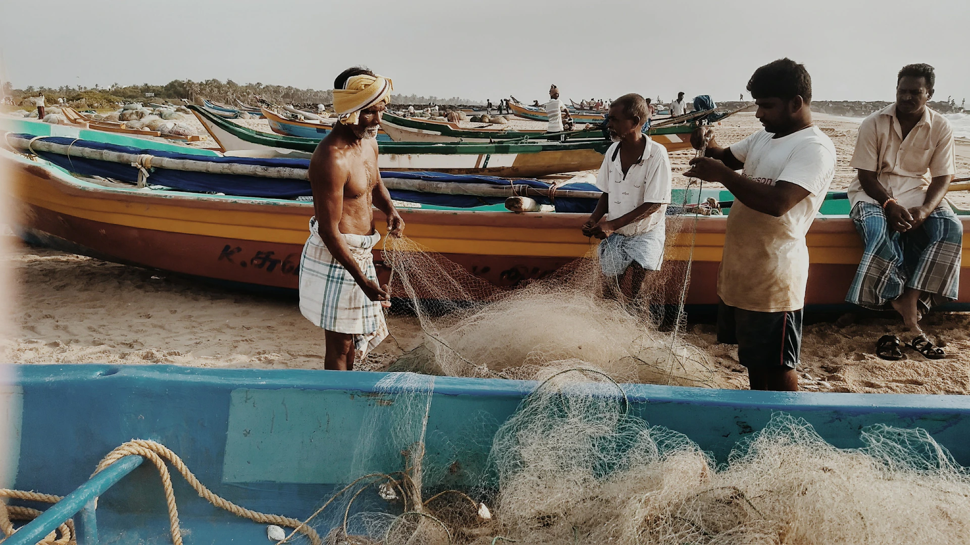 A close-up of colorful local fishermen preparing their nets beside traditional wooden pirogues on a sandy shore.