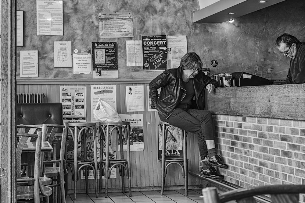 woman sits on bar stool near male cashier inside the bar