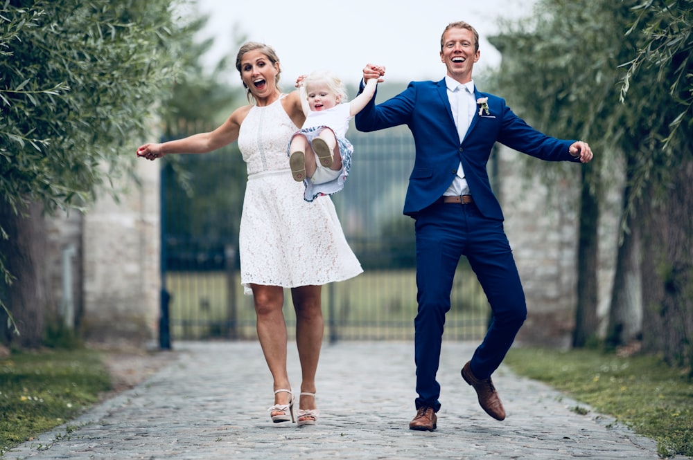 woman and man swinging a toddler by their arms during day