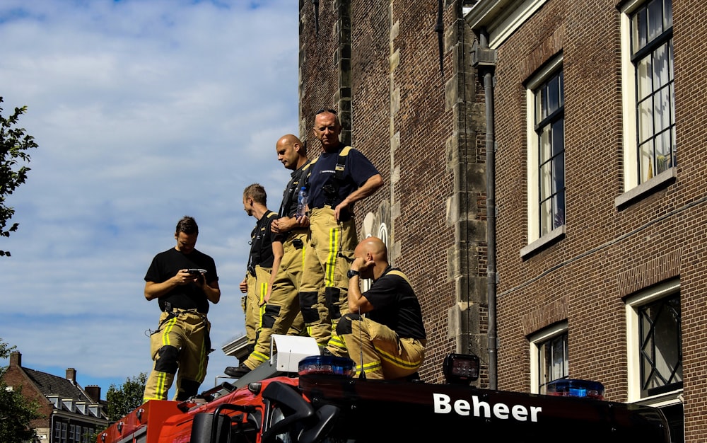firemen on top of firetruck near brown building under white and blue sky during daytime