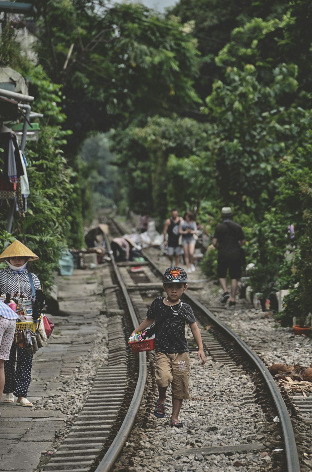 boy walking on train railway surrounded with tall and green trees during daytime