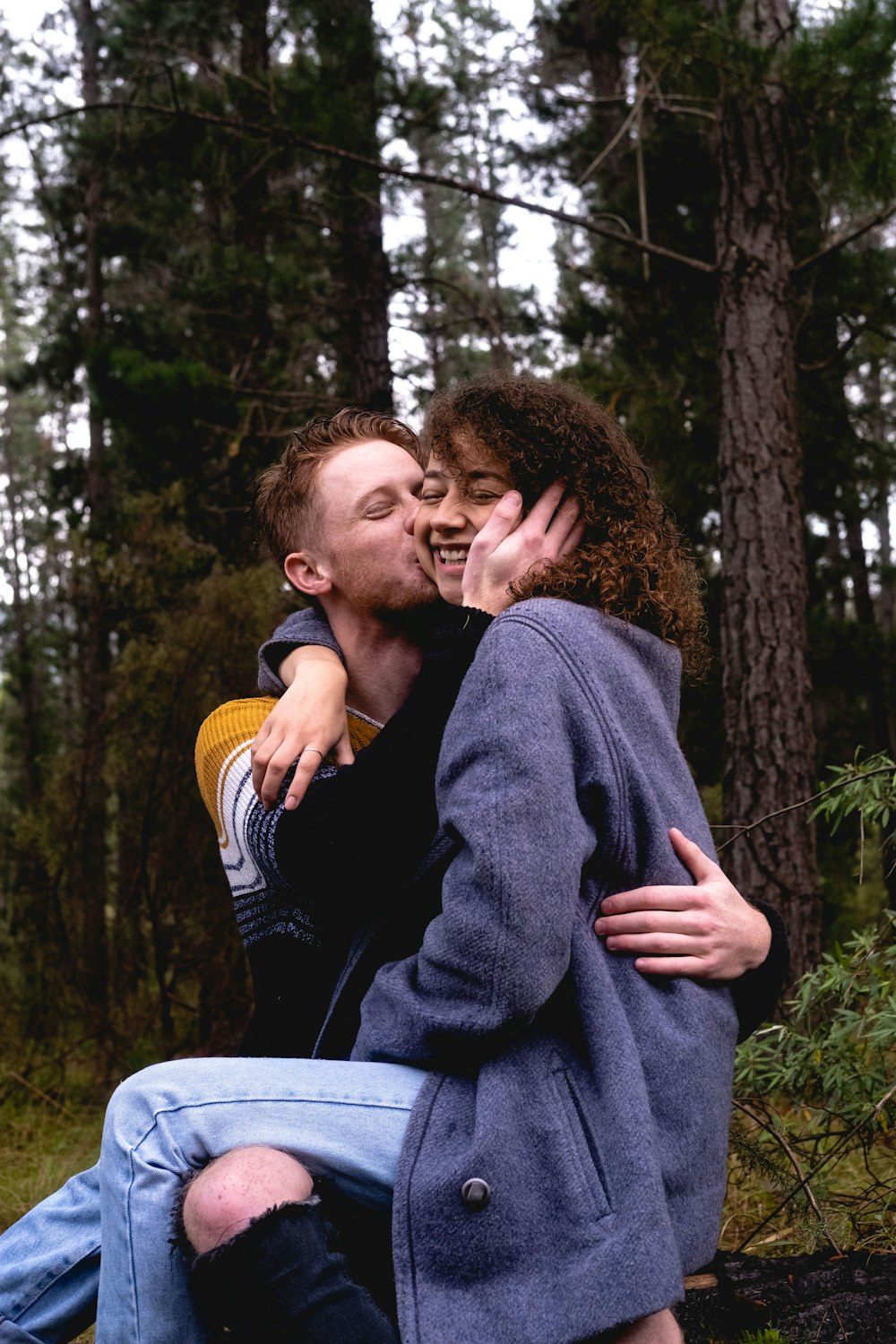 man kissing woman sitting on his lap near trees during day