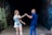 A man and a woman are dancing together in a dimly lit tunnel. The woman is wearing a colorful floral dress, and the man is dressed in a dark blue shirt and jeans. Graffiti is visible on the walls of the tunnel, adding an urban feel to the scene.