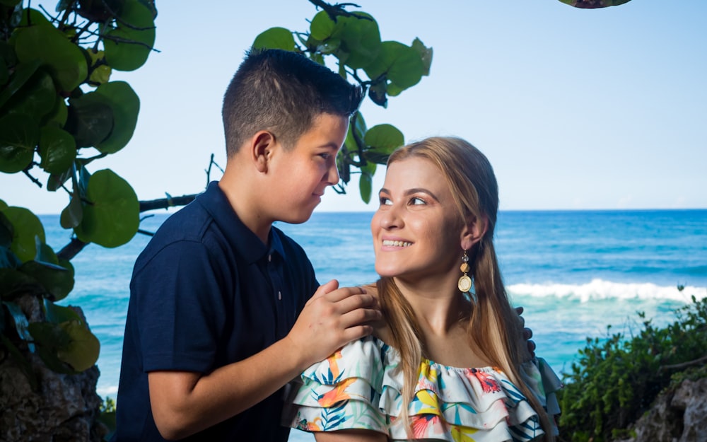 a woman and a boy standing next to each other near the ocean