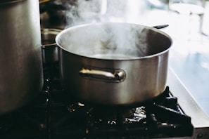 A stainless steel pot simmering on a stove with fresh herbs beside it.