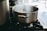 Close-up of a shiny stainless steel saucepan with steam rising, on a kitchen stove.