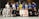 A group of people dressed in martial arts uniforms, likely participating in a Brazilian Jiu-Jitsu class, posed together for a group photo in a dojo or gym with exercise equipment in the background. The mix of uniforms includes various colors such as white, blue, black, pink, and yellow.