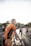 Several cyclists are gathered on a road wearing matching orange and black cycling jerseys. Each person appears to be preparing for a ride, holding their bicycles. The light from the sunrise or sunset creates a bright, warm atmosphere.