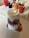An upside-down plastic cup with multicolored paint drips on a canvas, surrounded by other cups filled with different colors of paint. The paint has spilled out from the cup, creating an intriguing mix of colors. The scene suggests a paint-pouring art activity.