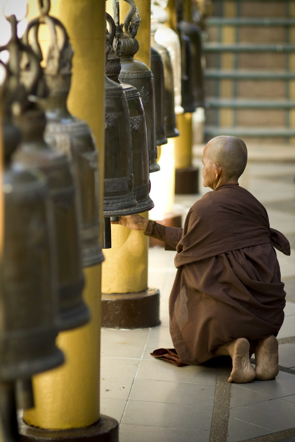 monk kneeling in front of gray bell