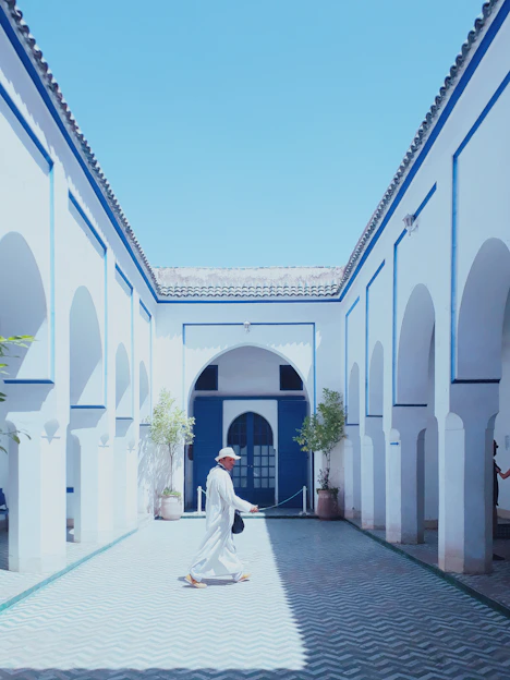 A traditional South Indian man dressed in an elegant white dhoti and angavastram, standing in a sunlit courtyard.