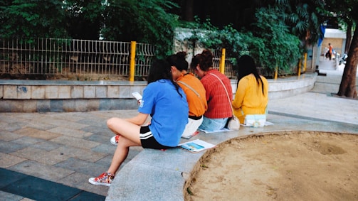A diverse group of people reading newspapers and using digital devices outdoors.