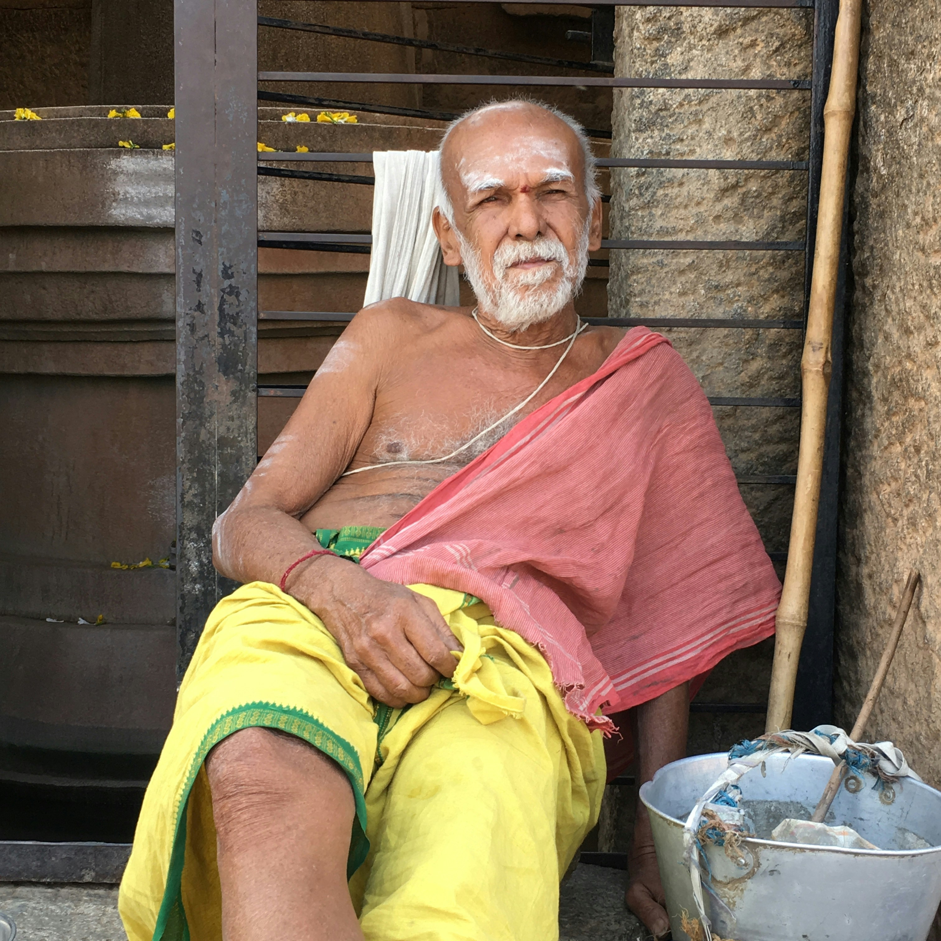 Elderly man sitting quietly on stone steps, shadow falling across half his face, serene expression