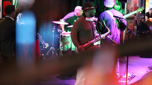 A jazz band performing on stage, with musicians playing instruments such as the saxophone, drums, and guitar. The scene is set in a dimly lit venue with colorful lighting and a lively atmosphere.