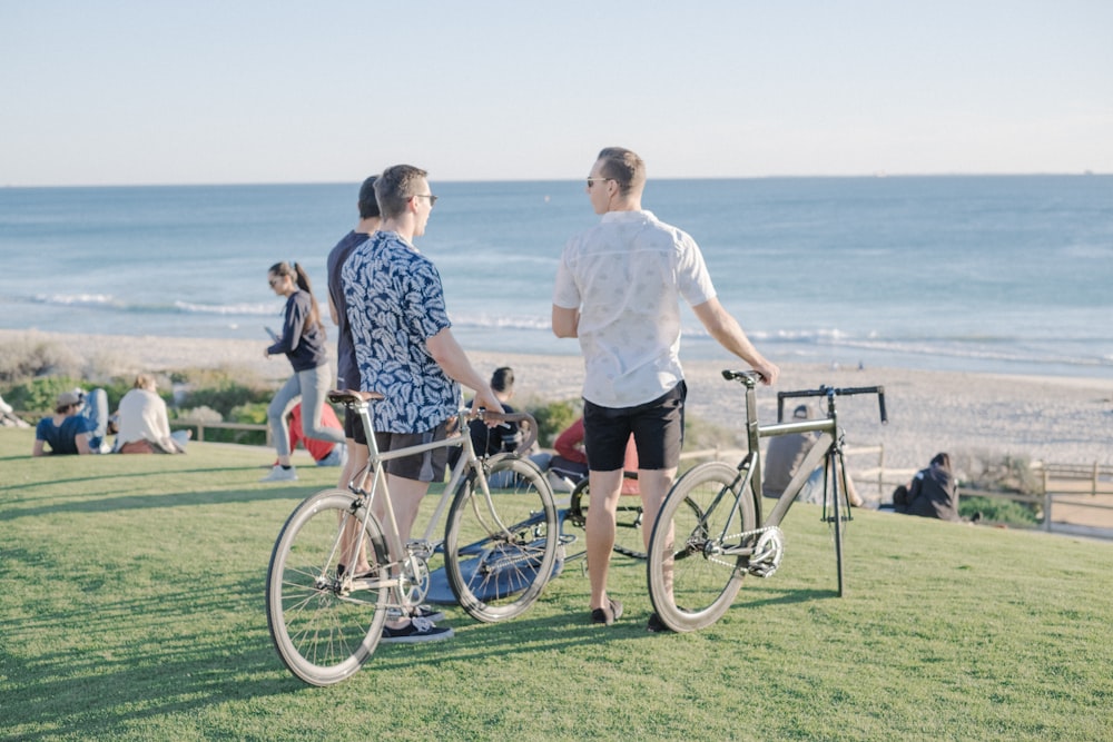 Tres hombres con bicicletas de cercanías en un campo de hierba frente al mar