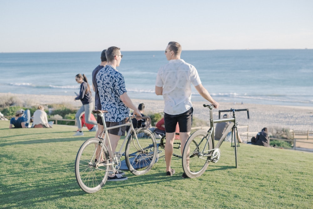 Tre uomini con biciclette pendolari sul campo d'erba di fronte al mare