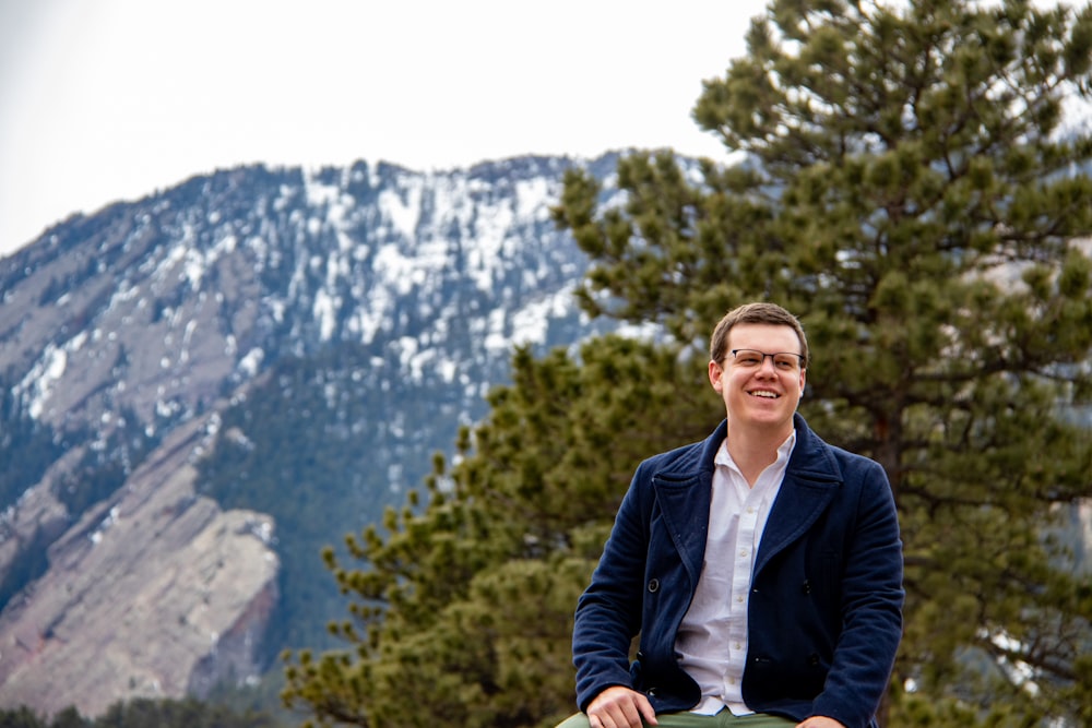 man in blue blazer sitting in front of green tree