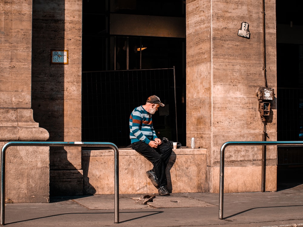 man sitting on wall beside road