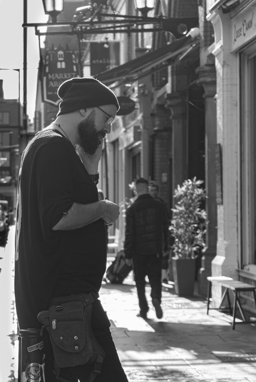 grayscale photo of man on sidewalk using phone