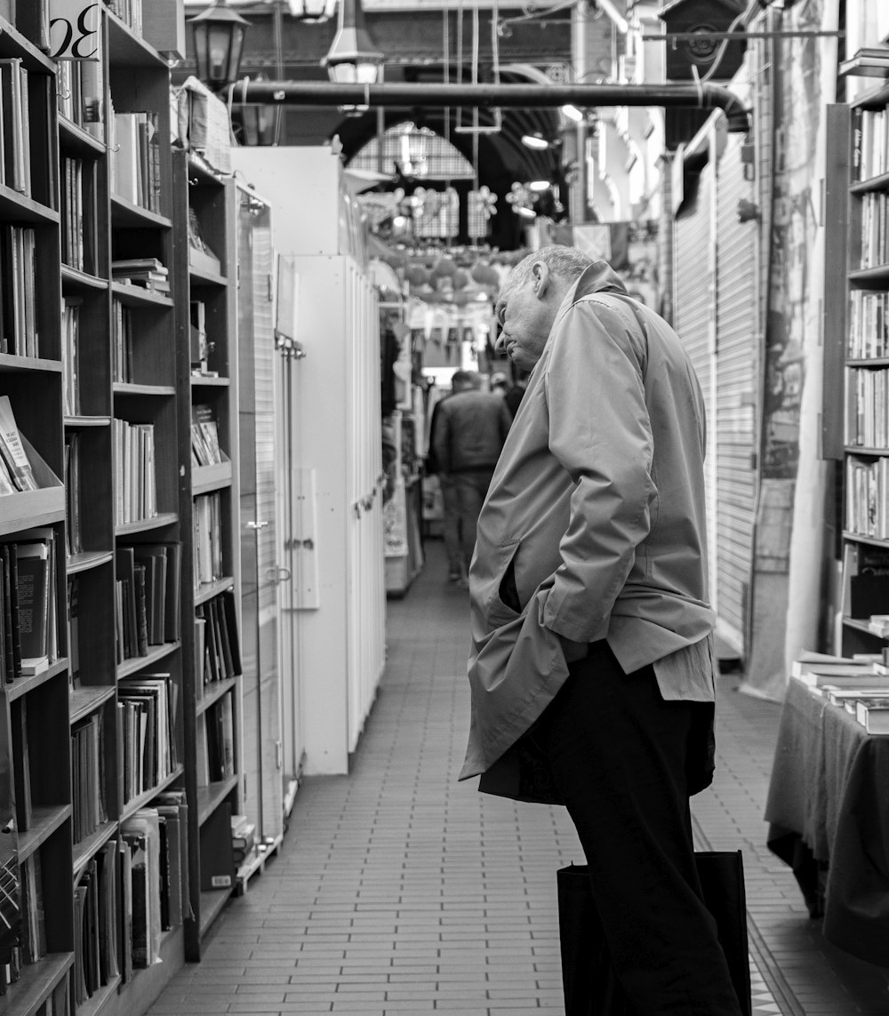 grayscale photo of man looking at bookshelves