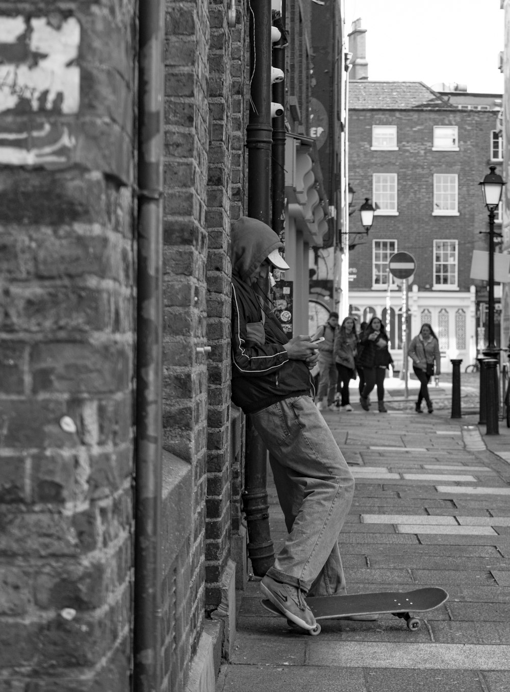 grayscale photo of man with skateboard leaning on wall