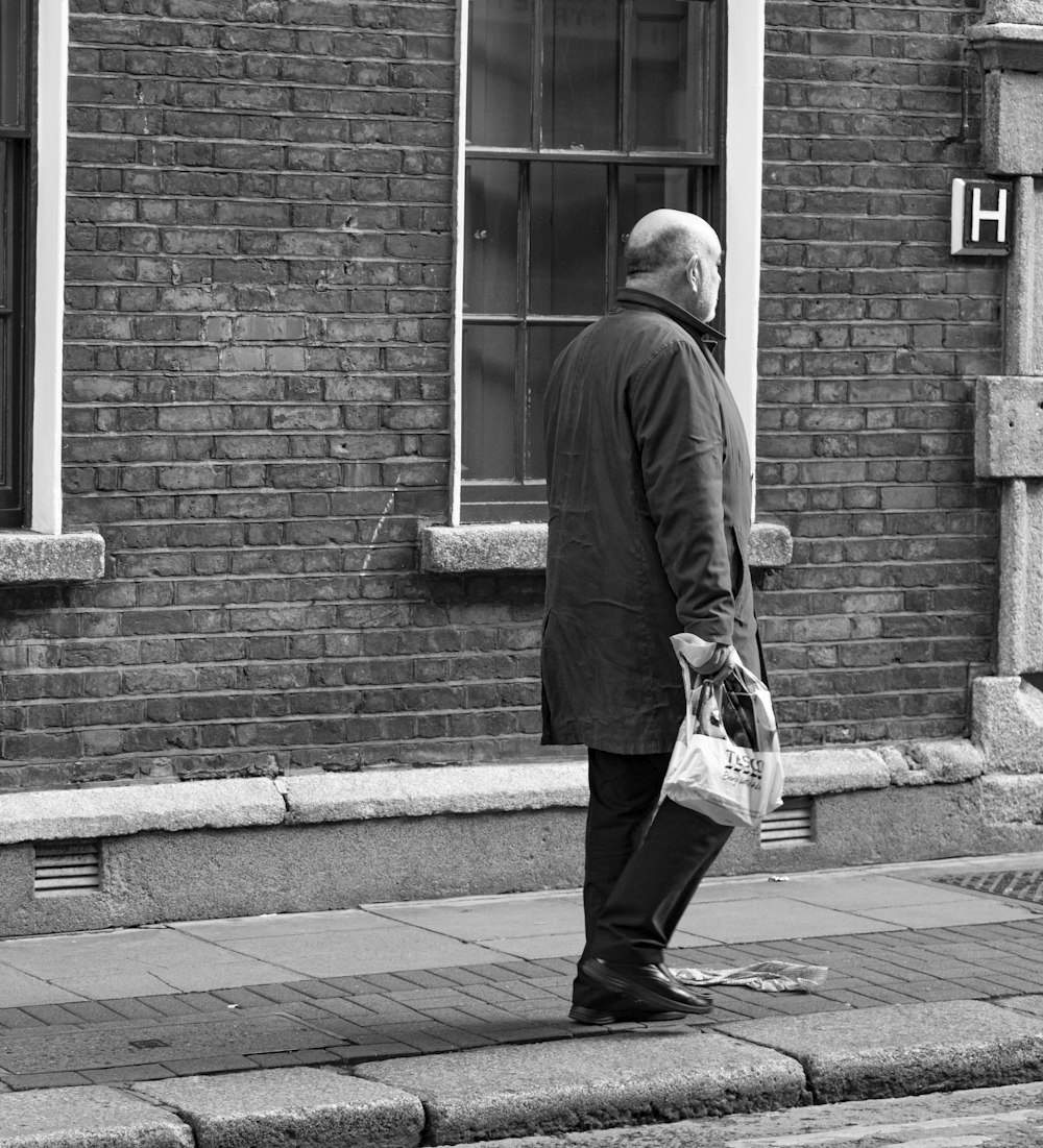 grayscale photo of man walking on sidewalk