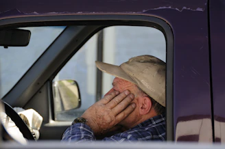 A tired driver resting inside his parked truck, reflecting on work conditions.