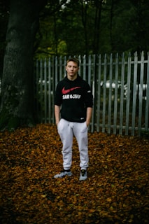 An athlete wearing a Karpatyman hoodie, standing on a forest trail with autumn leaves swirling around.