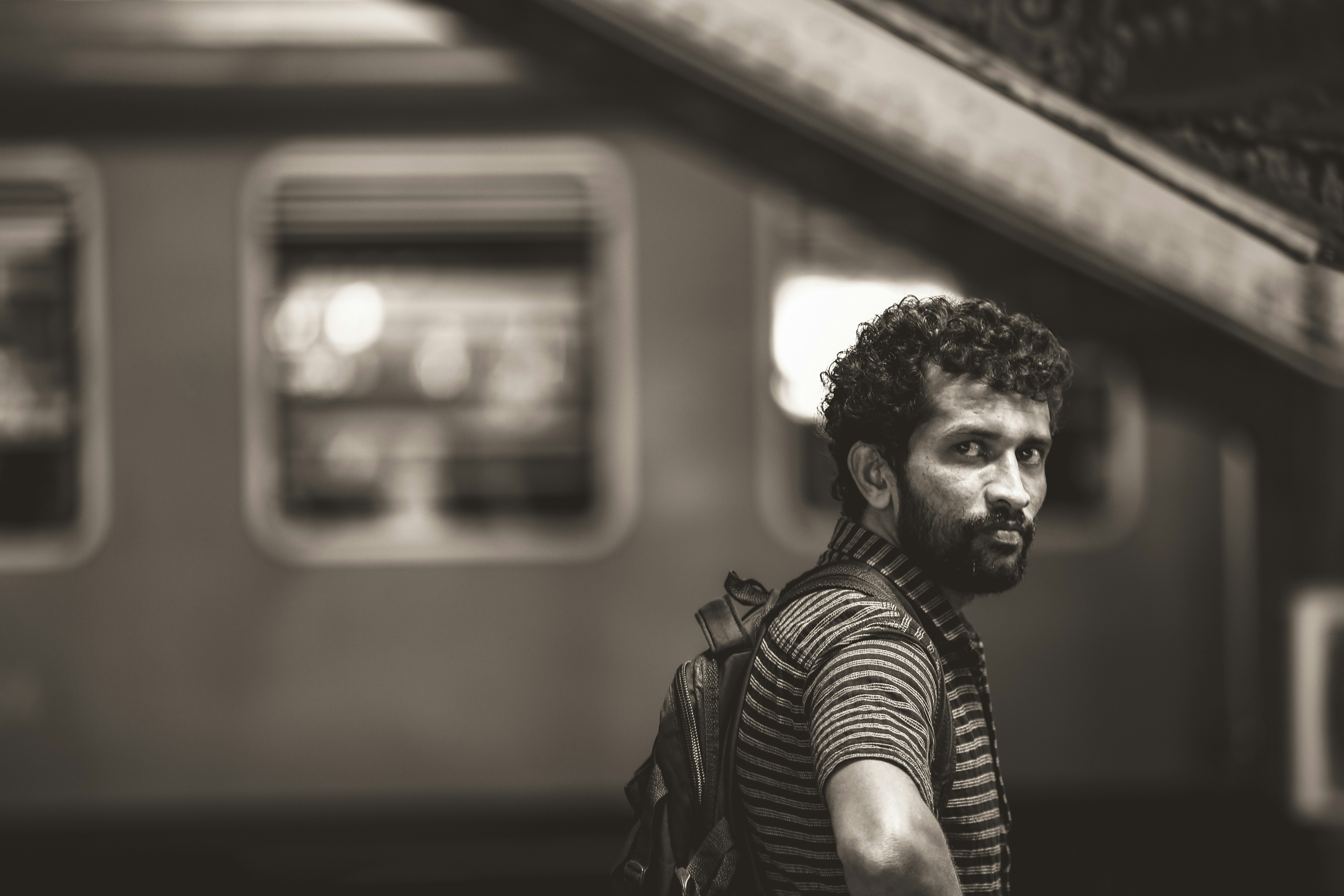 grayscale photography of man wearing striped shirt with backpack standing