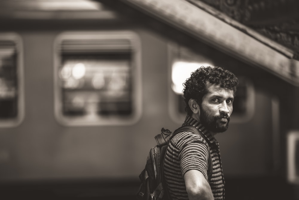 grayscale photography of man wearing striped shirt with backpack standing