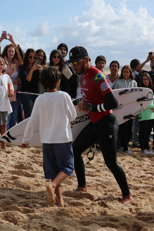 man walking with surfboard beside walking boy near people during day in Peniche Portugal