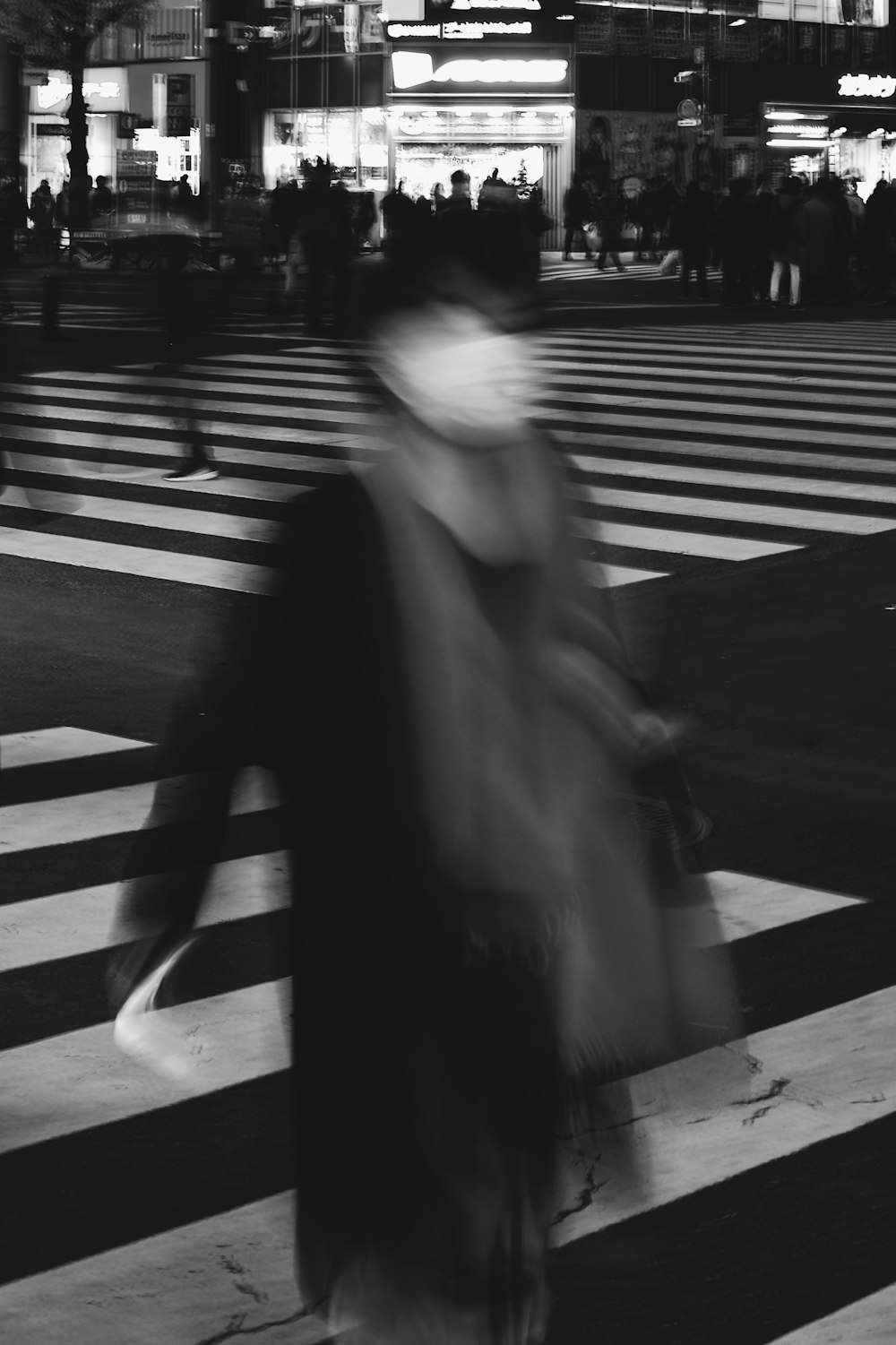 Foto en escala de grises de una mujer con abrigo negro caminando por el carril peatonal